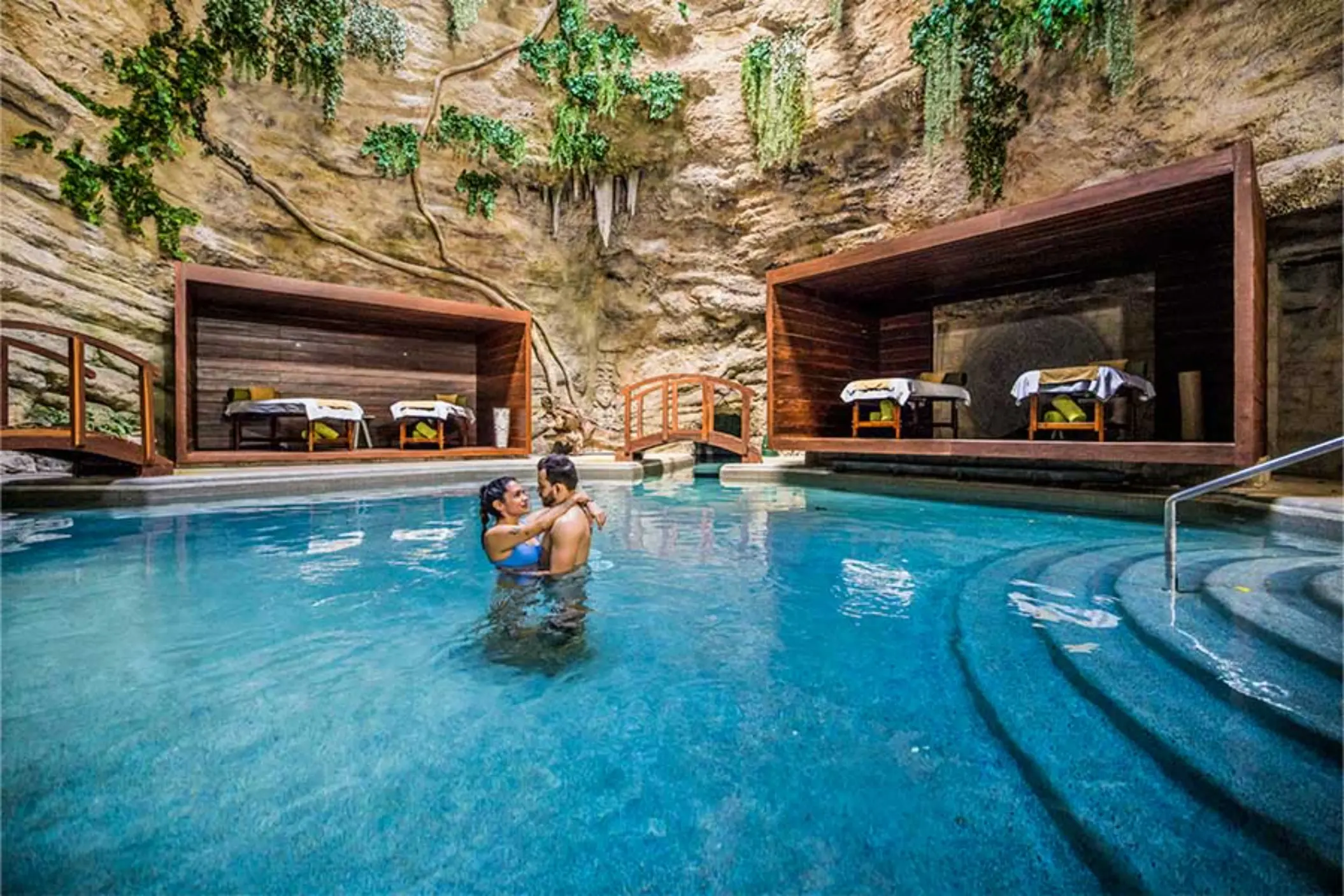 Romantic spa nestled in a natural cave with massage beds, water features, and lush hanging vines.