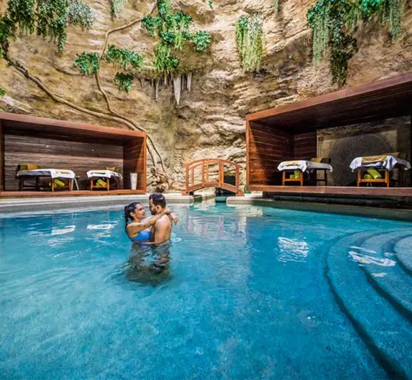 Romantic spa nestled in a natural cave with massage beds, water features, and lush hanging vines.