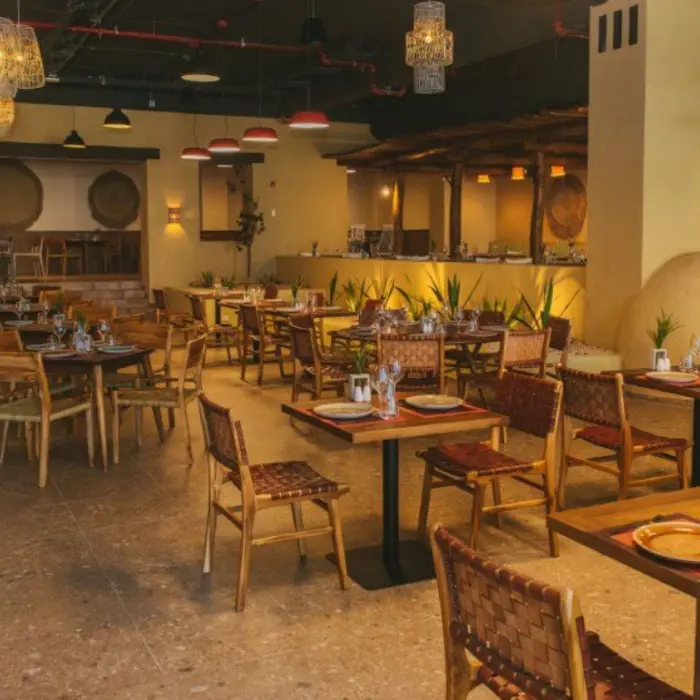 Rustic Mexican restaurant with earthy tones, cactus decor, woven chairs, and clay oven centerpiece.