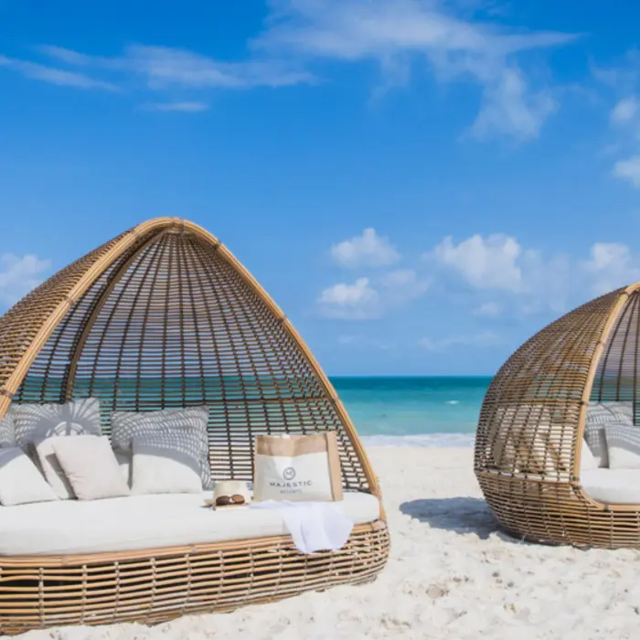 Stylish beach cabanas on white sand, shaded by wicker domes with ocean views and Majestic-branded accessories.