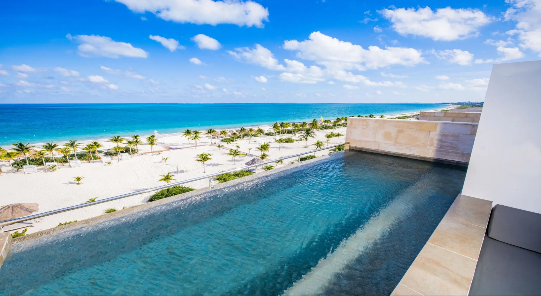 Modern suite at Majestic Elegance Costa Mujeres with king bed, sofa, and furnished balcony or swim-up access.