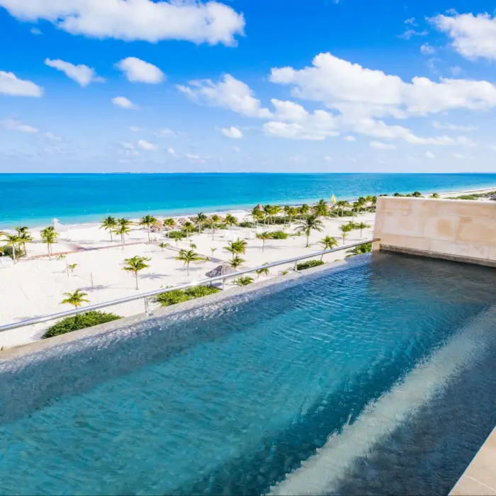 Modern suite at Majestic Elegance Costa Mujeres with king bed, sofa, and furnished balcony or swim-up access.