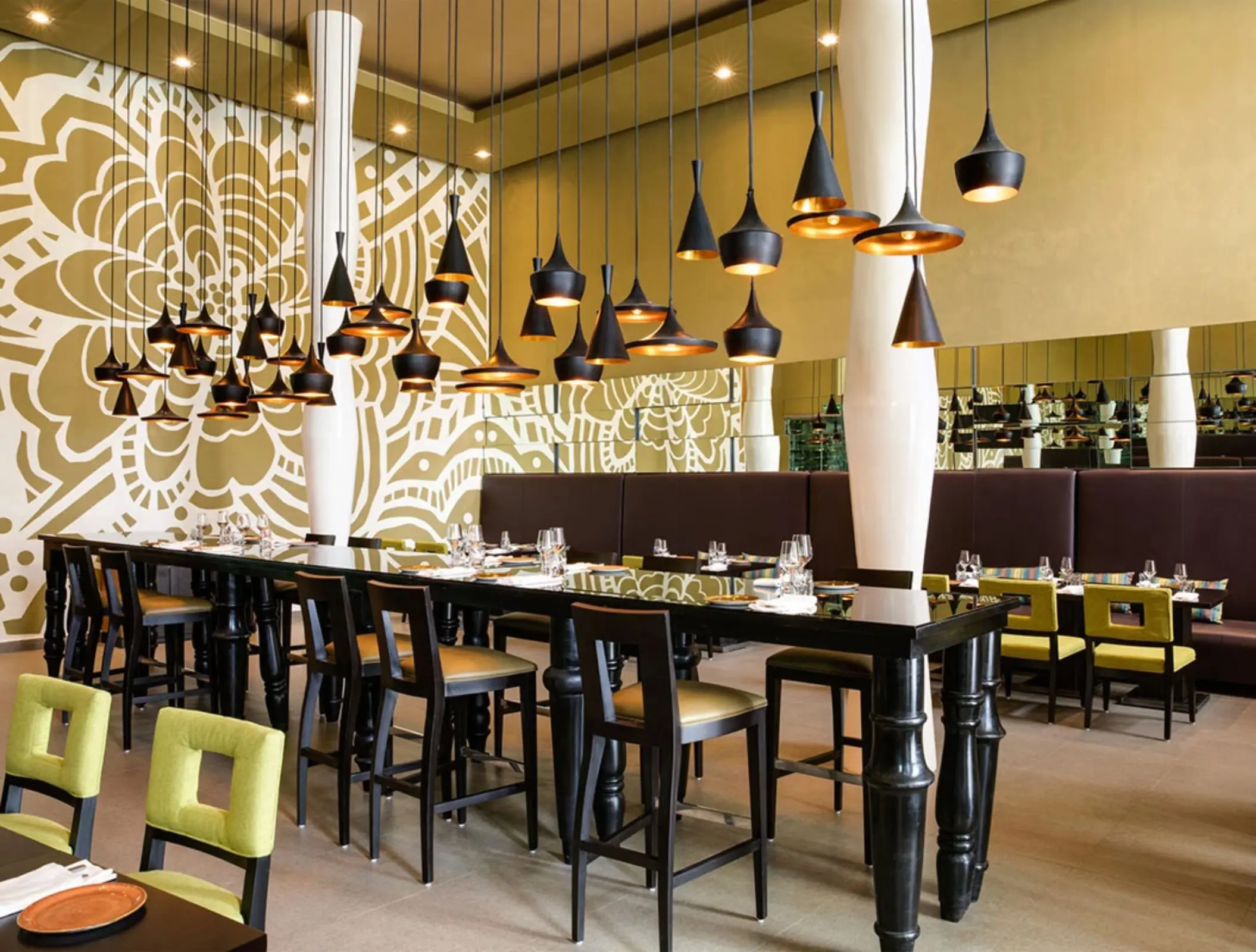 Stylish indoor restaurant with bold floral mural, black tables, green chairs, and modern hanging pendant lights.