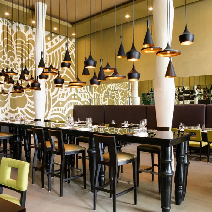 Stylish indoor restaurant with bold floral mural, black tables, green chairs, and modern hanging pendant lights.