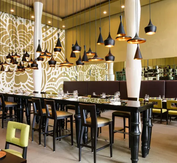 Stylish indoor restaurant with bold floral mural, black tables, green chairs, and modern hanging pendant lights.