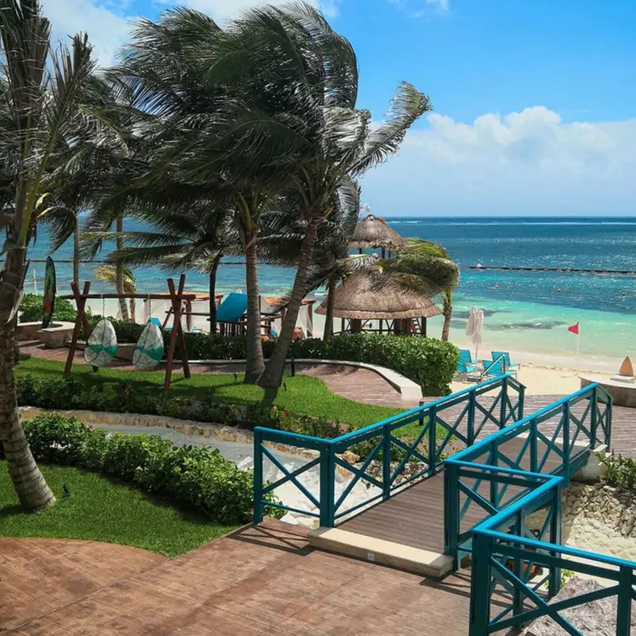 Oceanfront view with turquoise fences, palm trees, and cabanas overlooking a clear Caribbean sea.