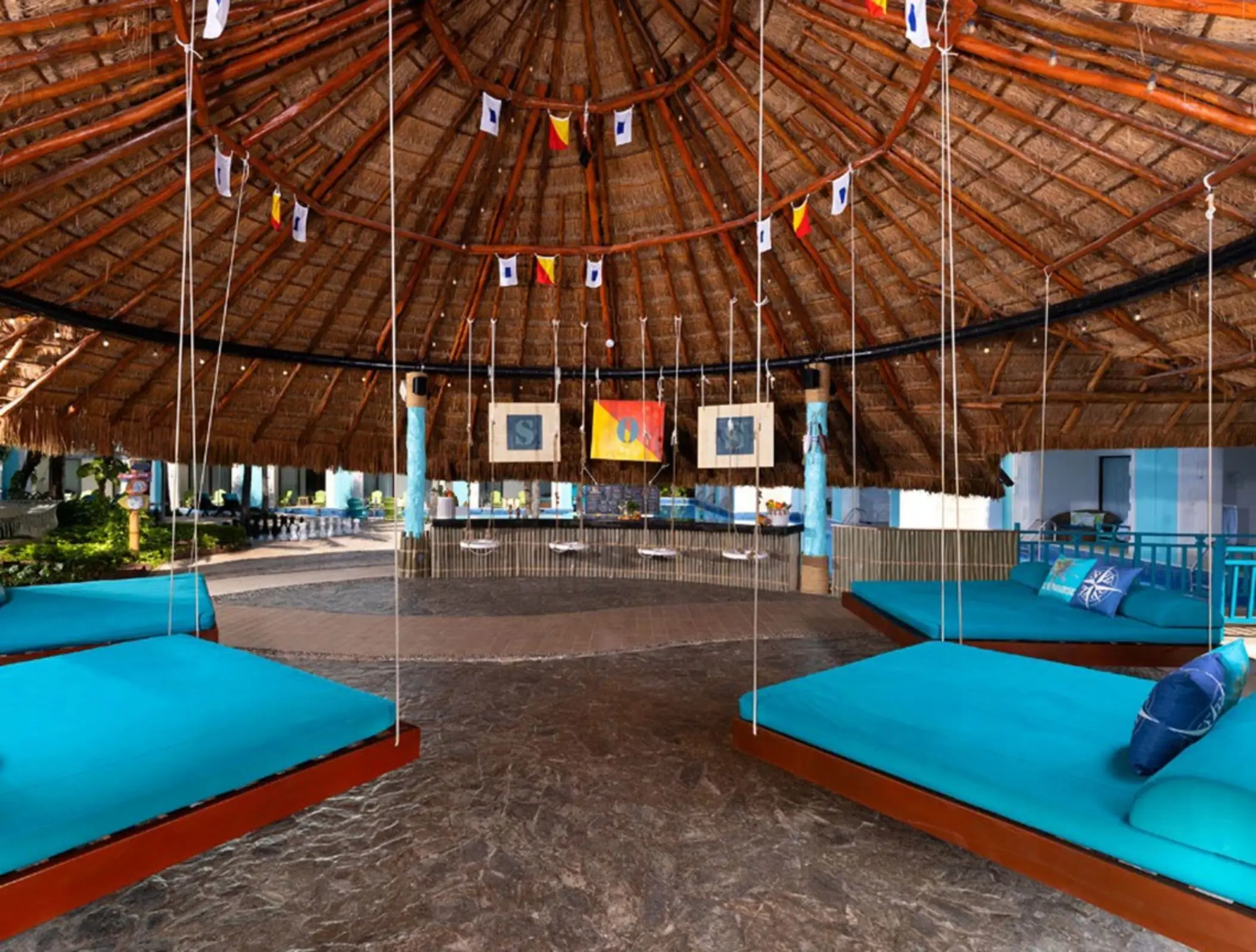 Open-air lobby lounge with hanging daybeds and a large thatched palapa roof at a beachfront resort.