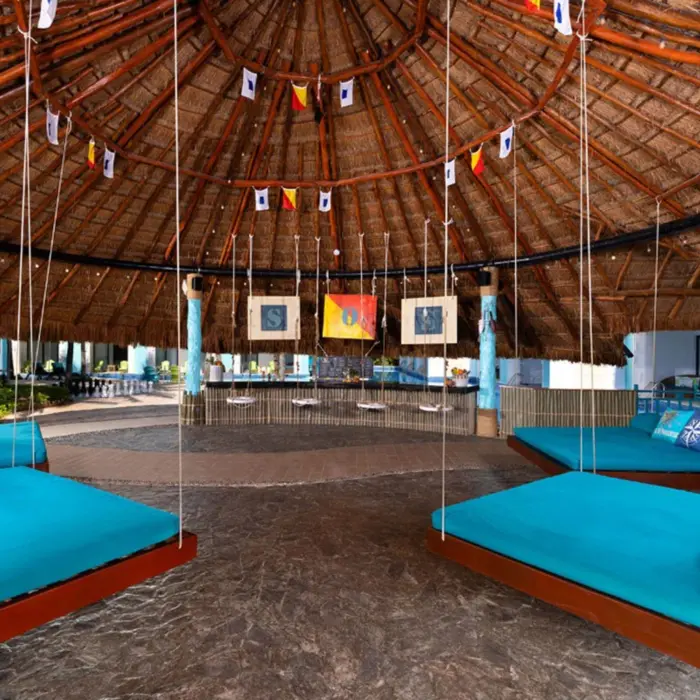 Open-air lobby lounge with hanging daybeds and a large thatched palapa roof at a beachfront resort.