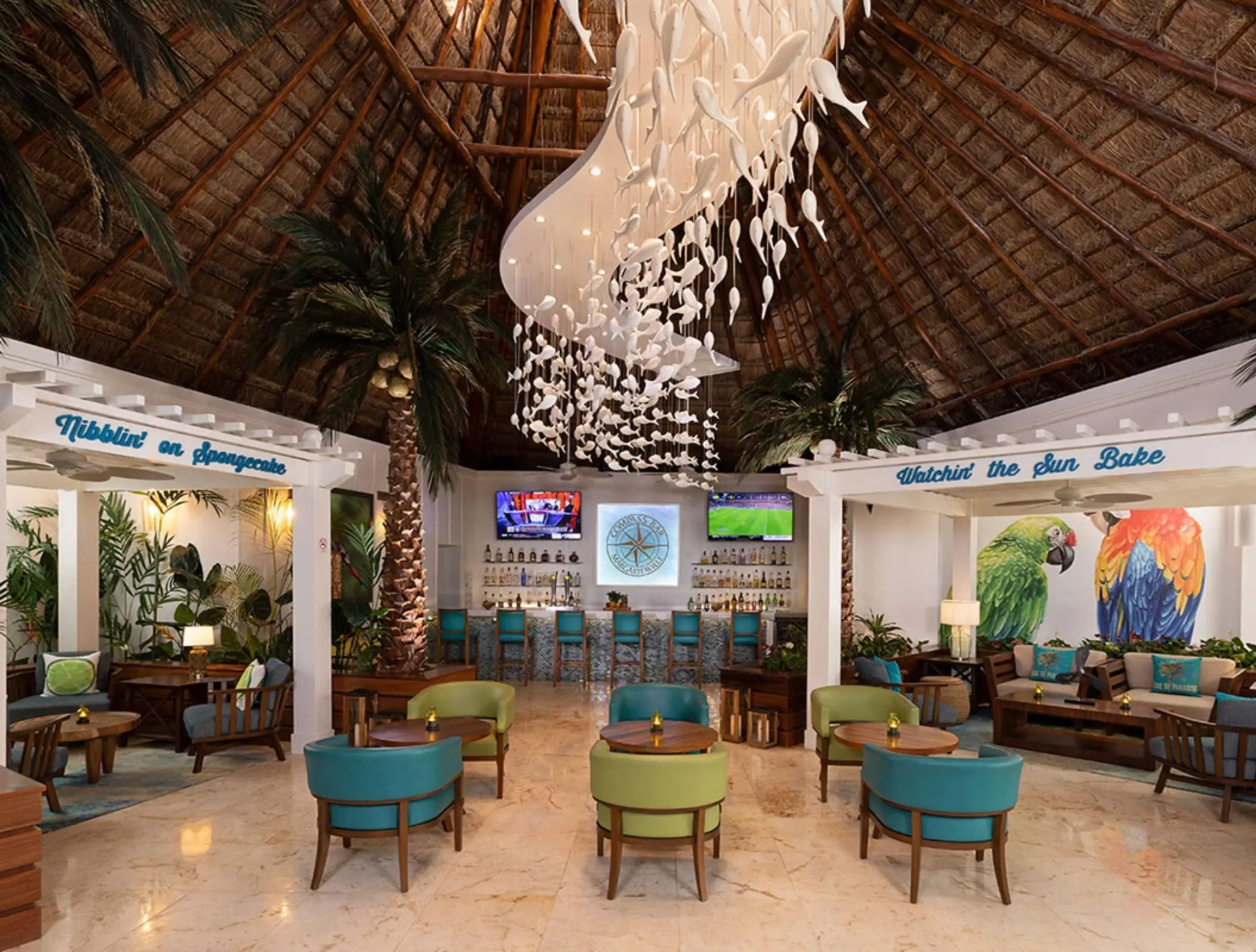 Colorful lobby bar with thatched ceiling, parrot murals, tropical decor, and vibrant lounge furniture.