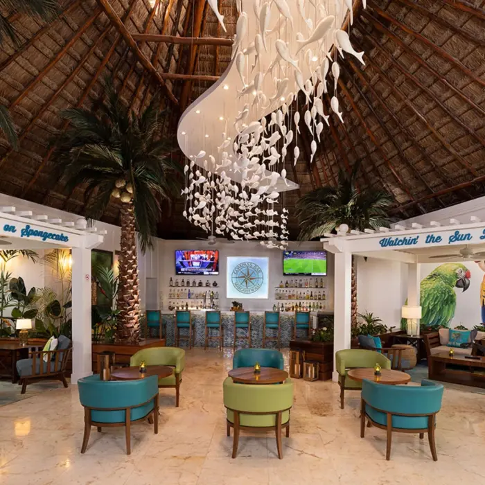 Colorful lobby bar with thatched ceiling, parrot murals, tropical decor, and vibrant lounge furniture.