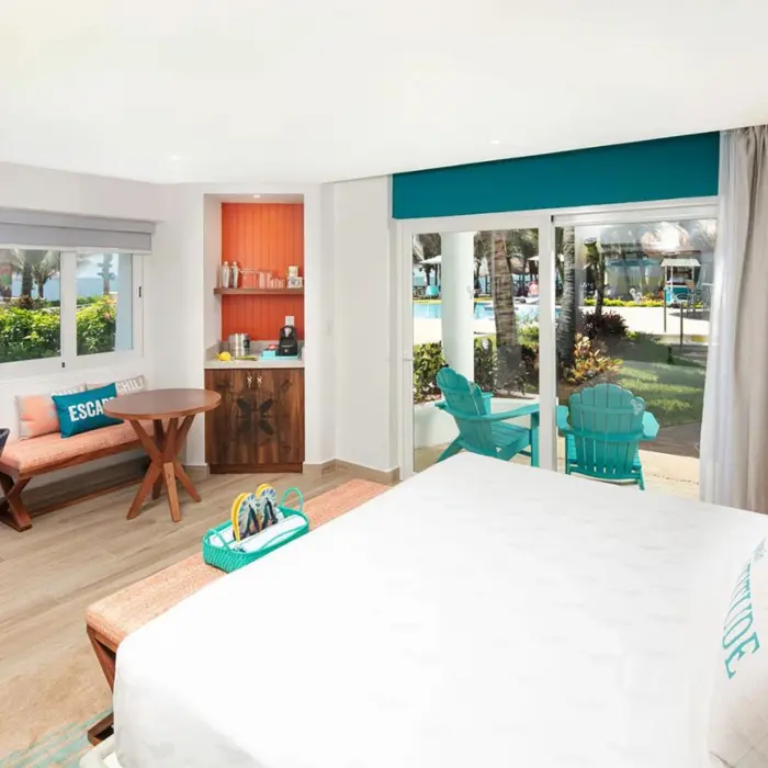 Bright and airy resort room with modern decor, king bed, outdoor terrace, and pool views through glass doors.
