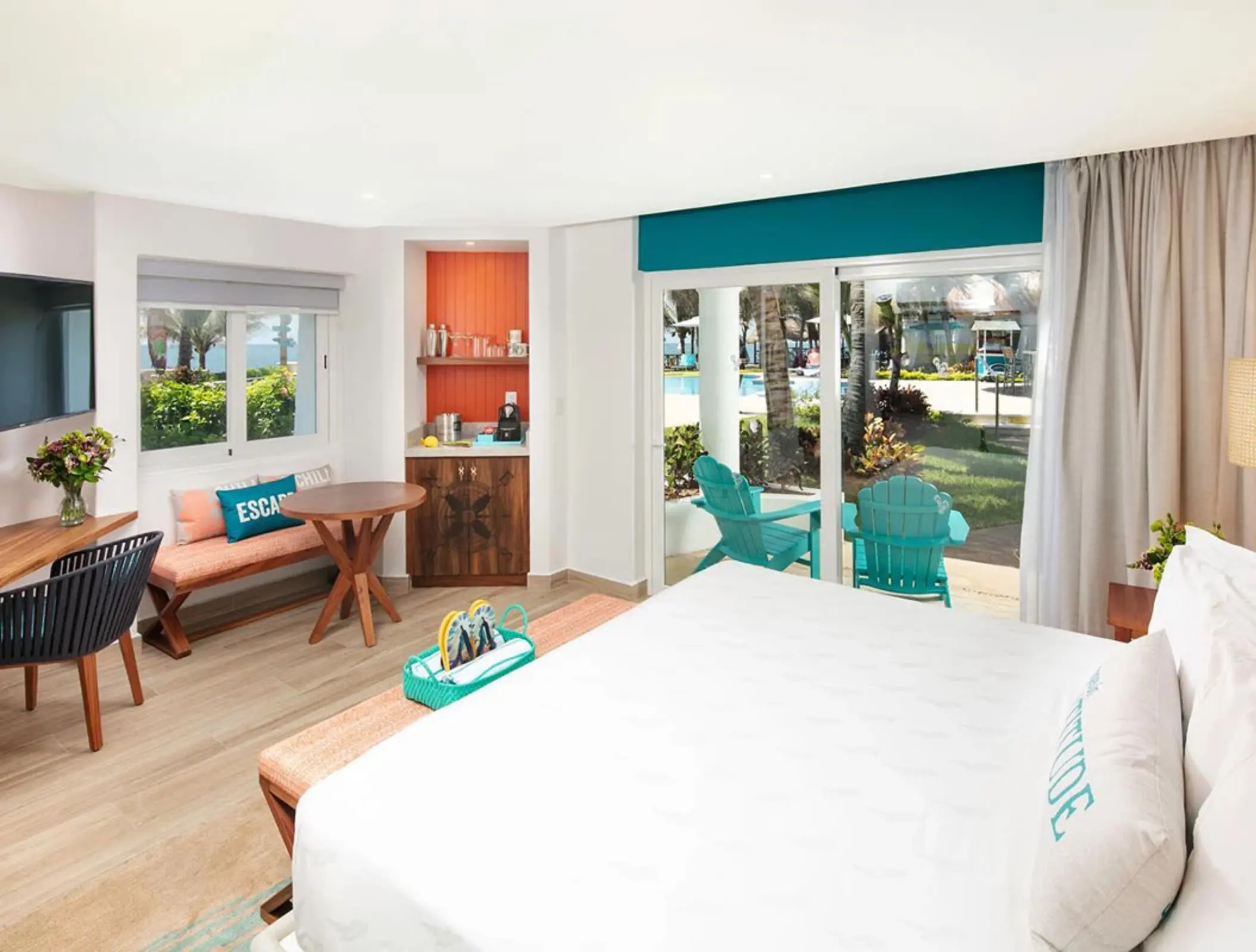 Bright and airy resort room with modern decor, king bed, outdoor terrace, and pool views through glass doors.
