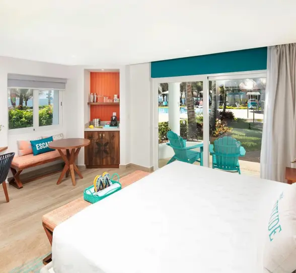 Bright and airy resort room with modern decor, king bed, outdoor terrace, and pool views through glass doors.