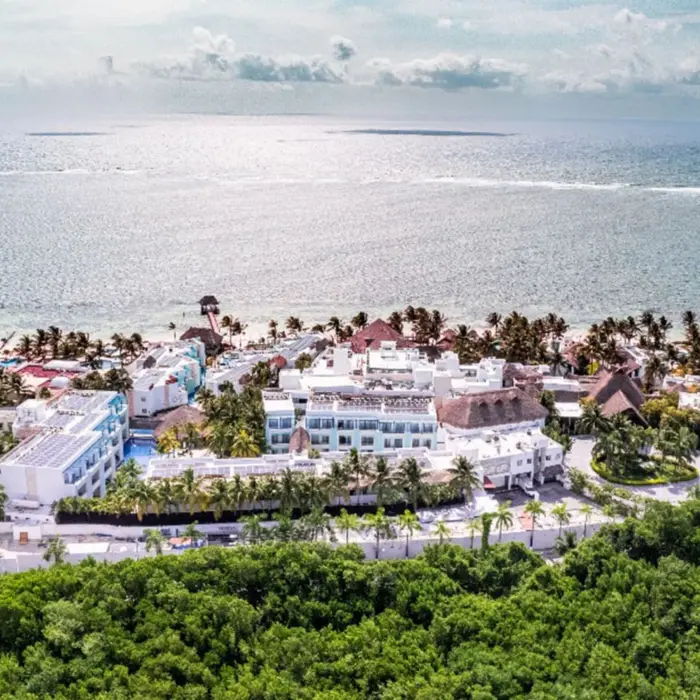 Aerial view of a beachfront resort with white buildings, lush palms, and the ocean stretching into the horizon.