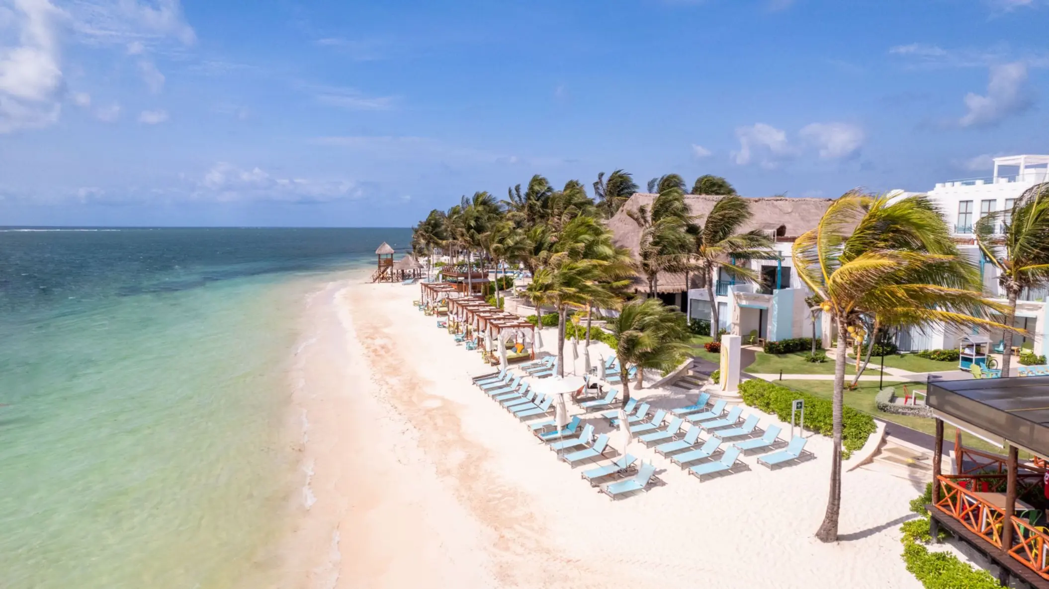 Sandy beach lined with turquoise lounge chairs and palm trees, facing the clear waters of the Caribbean Sea.