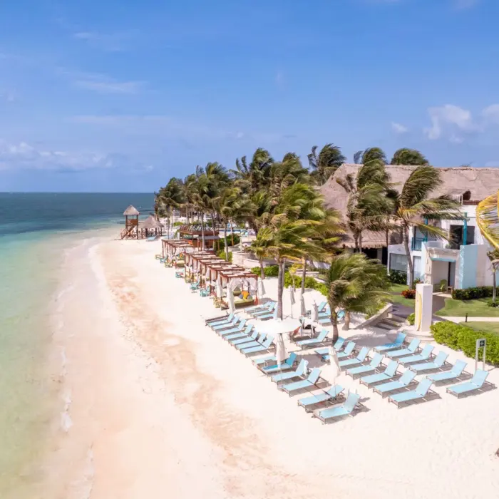 Sandy beach lined with turquoise lounge chairs and palm trees, facing the clear waters of the Caribbean Sea.