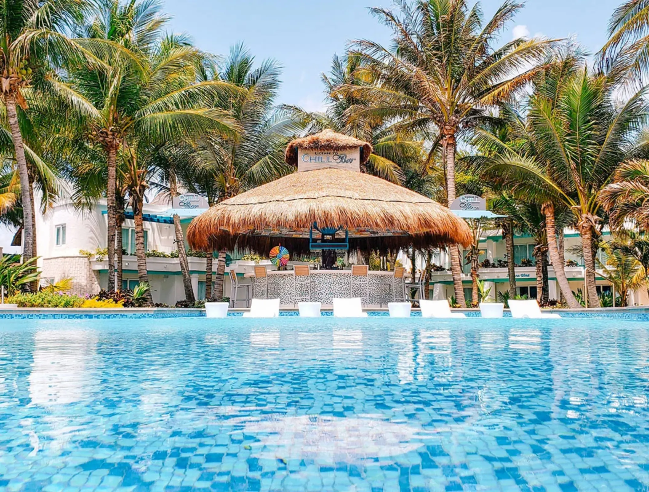 Swim-up bar with palapa roof and tropical palm trees surrounding a bright blue pool.