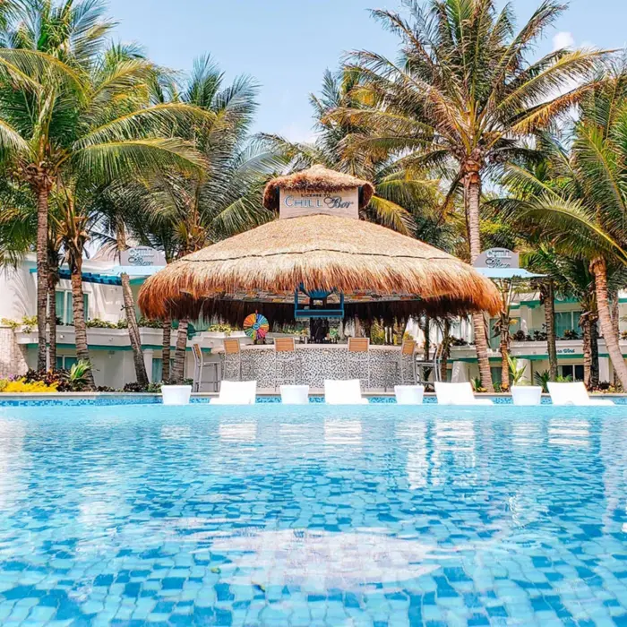 Swim-up bar with palapa roof and tropical palm trees surrounding a bright blue pool.