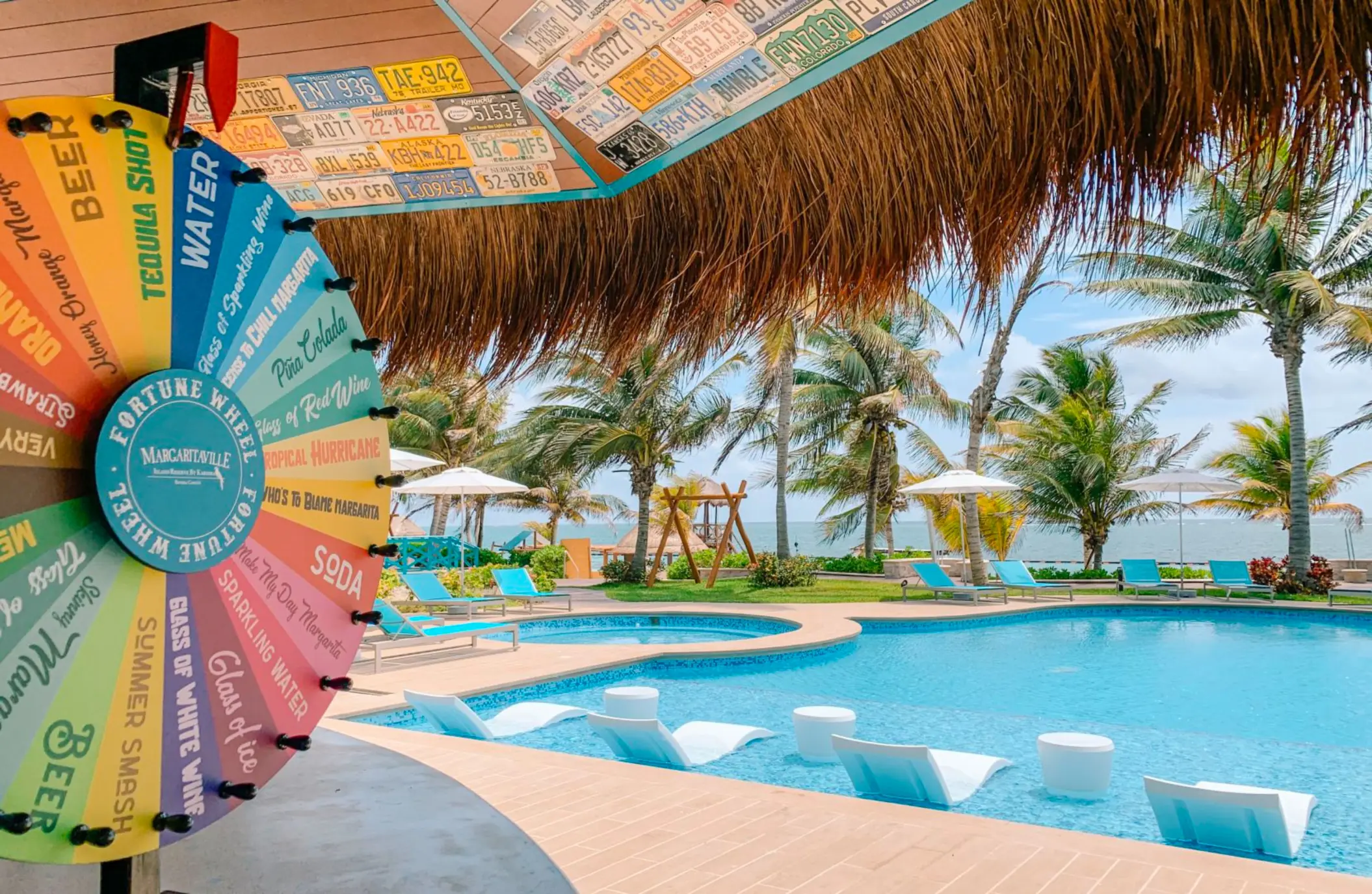 Colorful margarita wheel at bar overlooking poolside lounge chairs and ocean view.