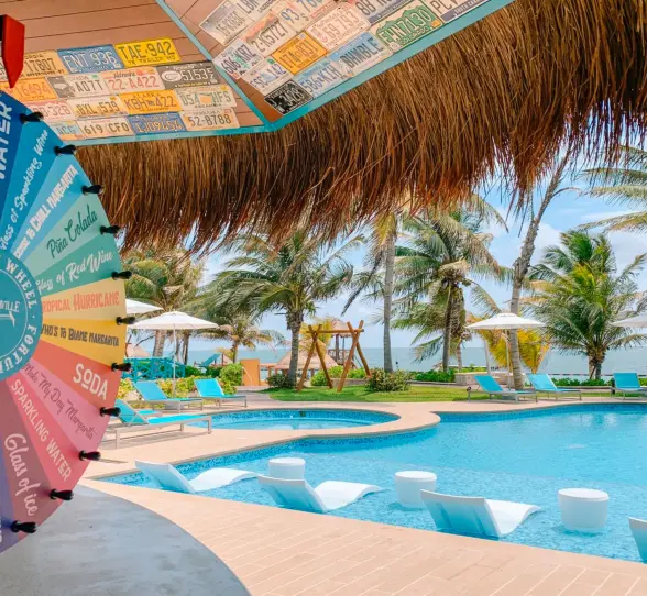 Colorful margarita wheel at bar overlooking poolside lounge chairs and ocean view.