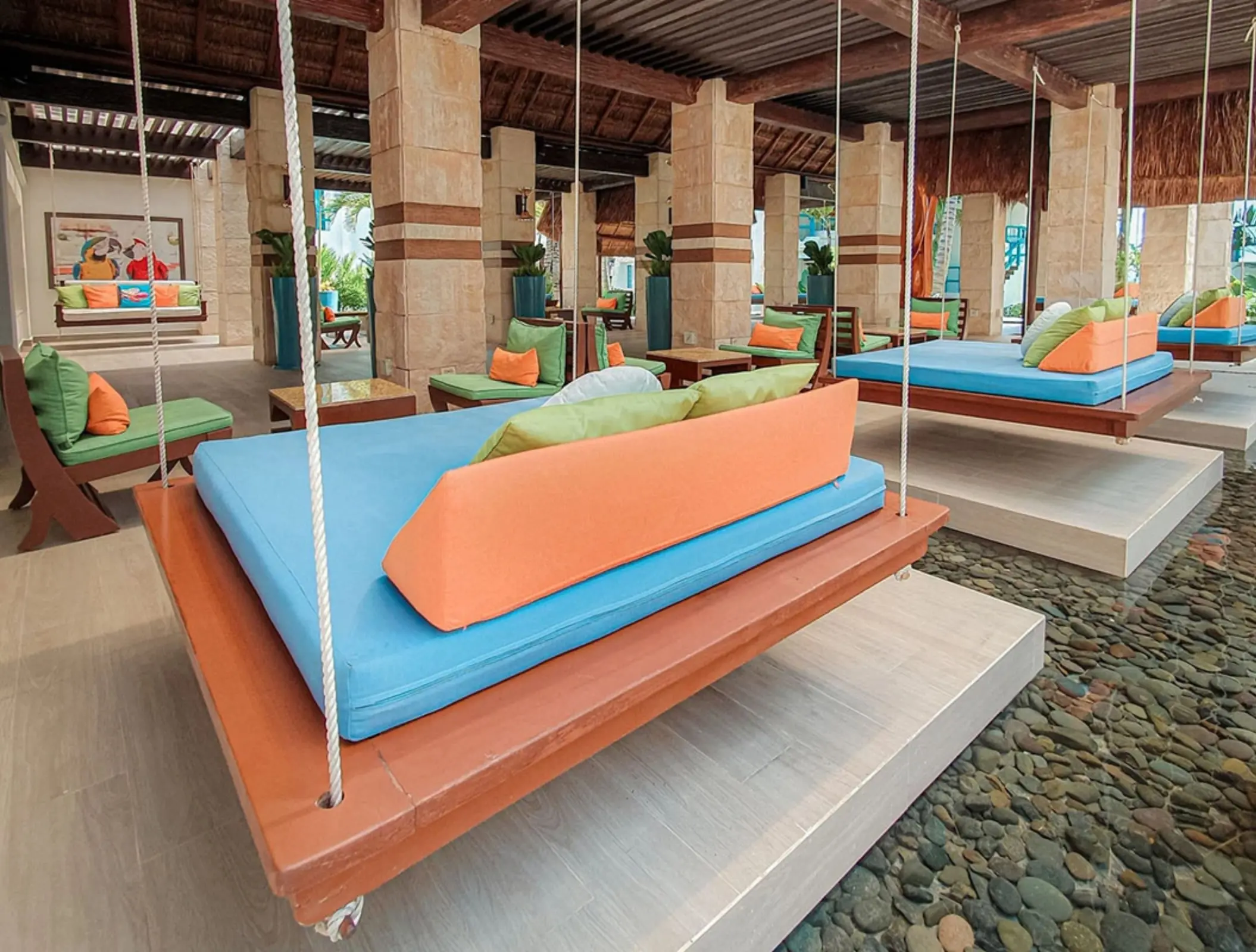 Colorful hanging daybeds over water inside open-air lounge with stone columns.