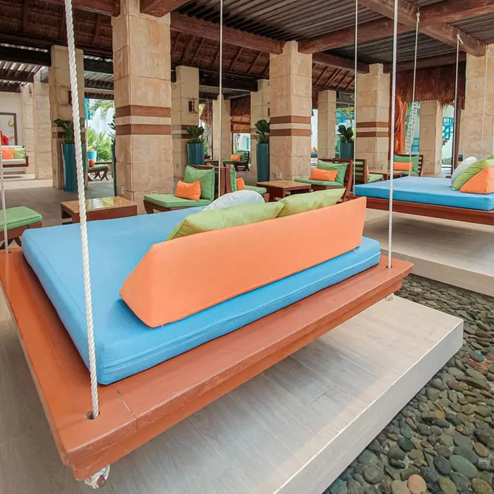 Colorful hanging daybeds over water inside open-air lounge with stone columns.