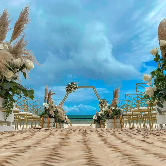 Romantic beach wedding setup with floral aisle, gold chairs, and hexagon arch.