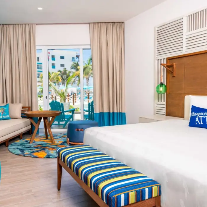 Spacious suite with king canopy bed, neutral tones, and patio access with views of lush tropical gardens.