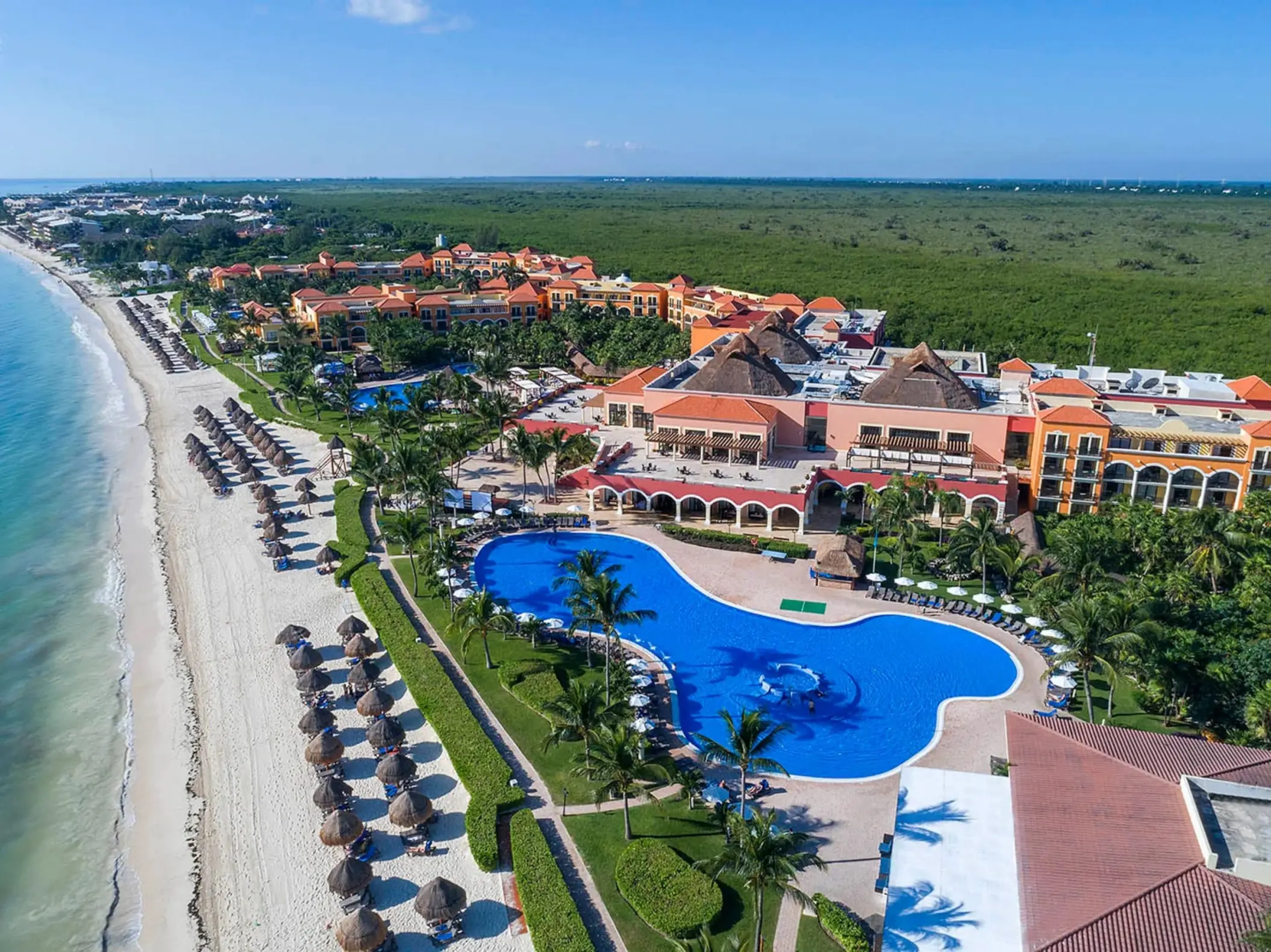 An aerial shot of the resort, showcasing the large winding pool, white sand beach, and ocean.