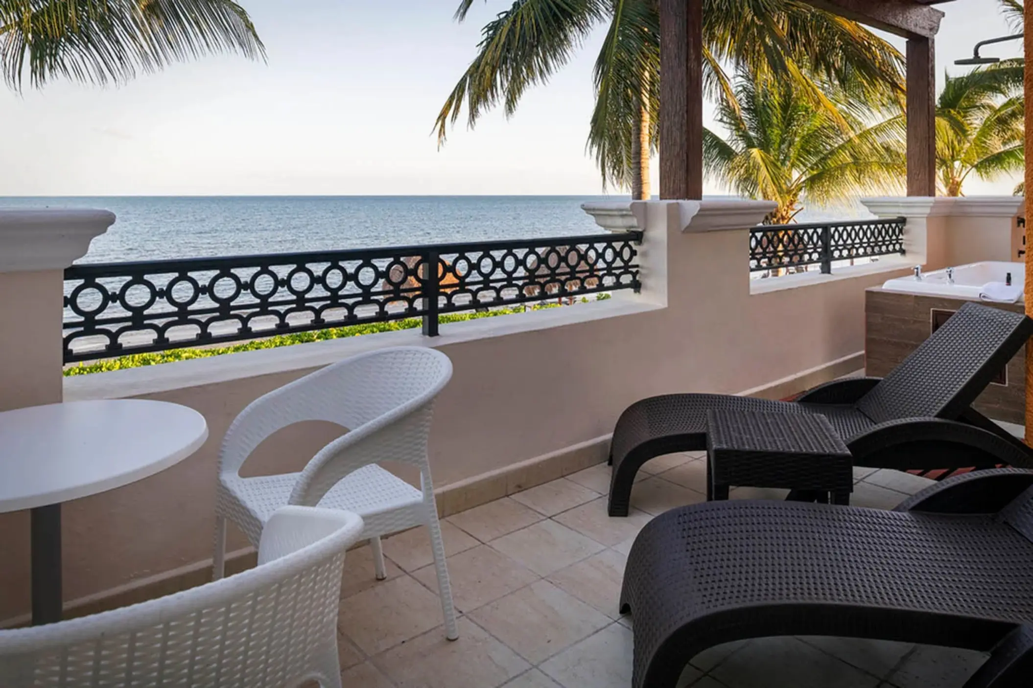 An ocean-view balcony with a private hot tub, lounge chairs, and a table with chairs.