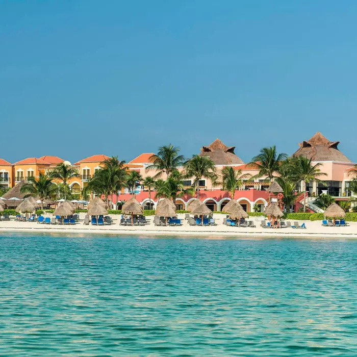 A wide shot of the resort's private beach with lounge chairs, palm trees, and the turquoise ocean.