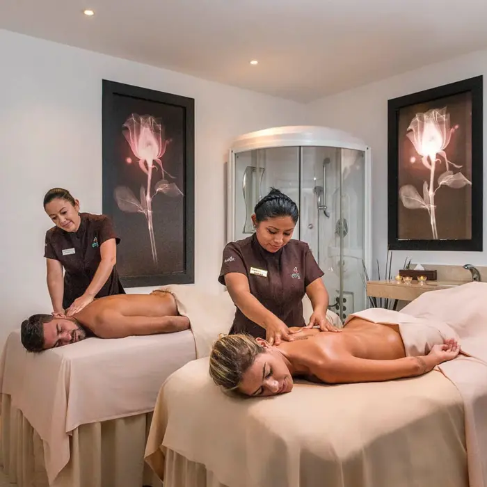 A couple getting massages side-by-side in a relaxing spa room with two therapists.