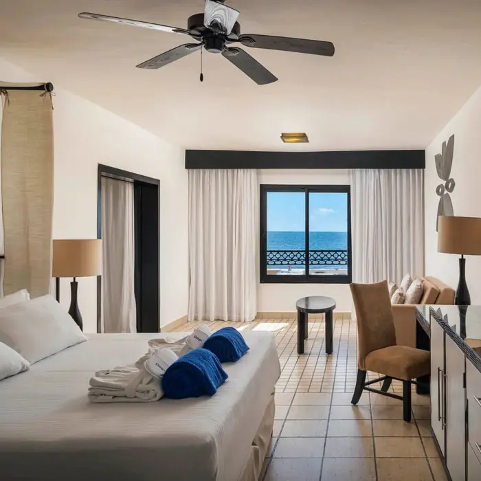A cozy honeymoon suite with a large bed, a ceiling fan, and a window with a stunning ocean view.