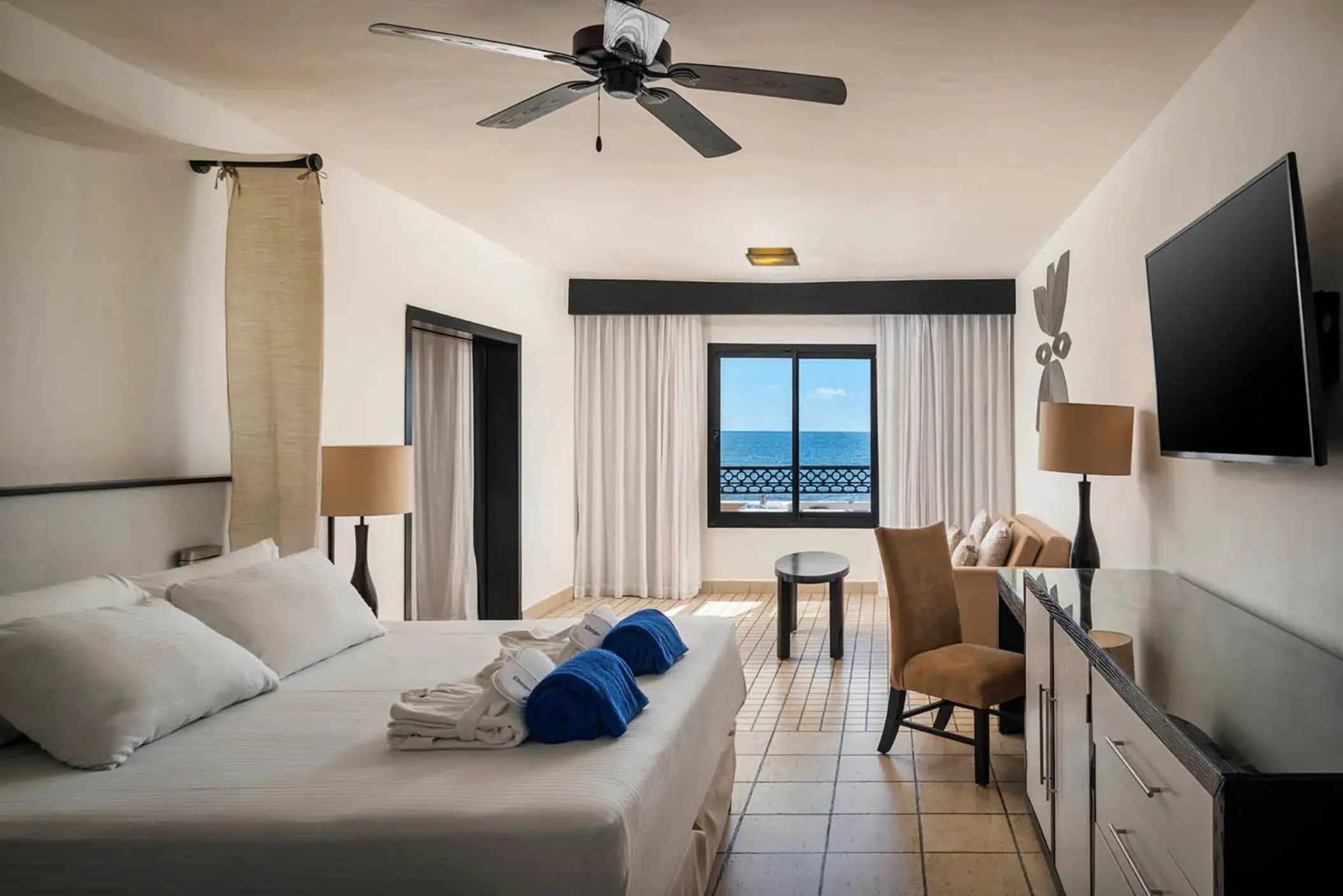 A cozy honeymoon suite with a large bed, a ceiling fan, and a window with a stunning ocean view.