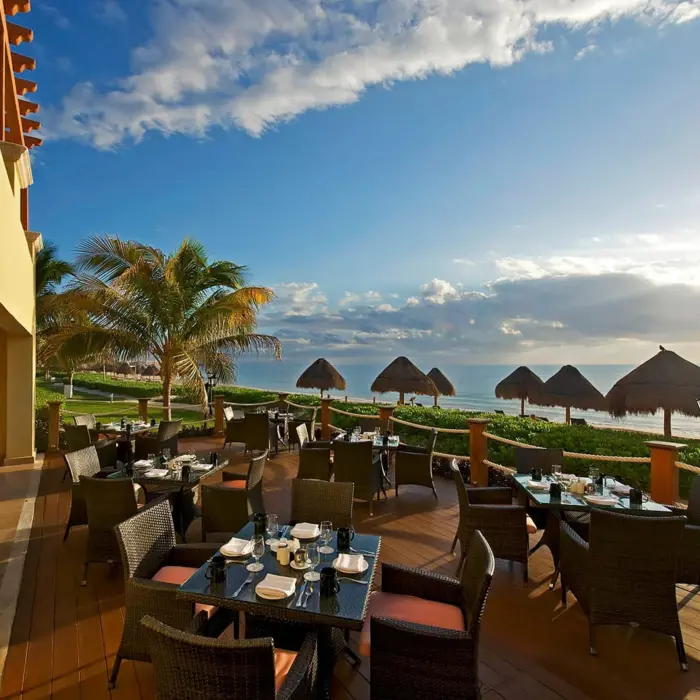 An outdoor terrace restaurant with tables and chairs, offering a beautiful view of the ocean.