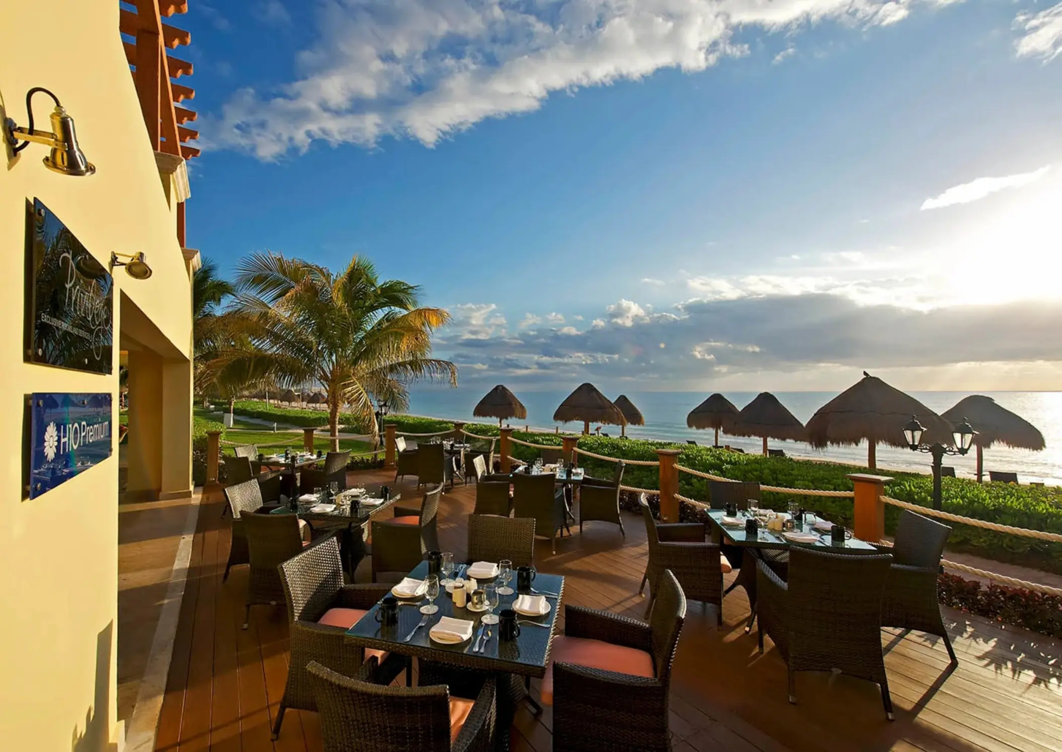 An outdoor terrace restaurant with tables and chairs, offering a beautiful view of the ocean.