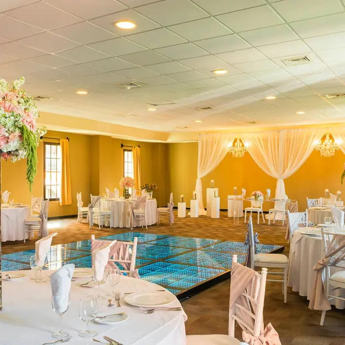 A reception hall decorated for an event, featuring tables with floral centerpieces and a dance floor.