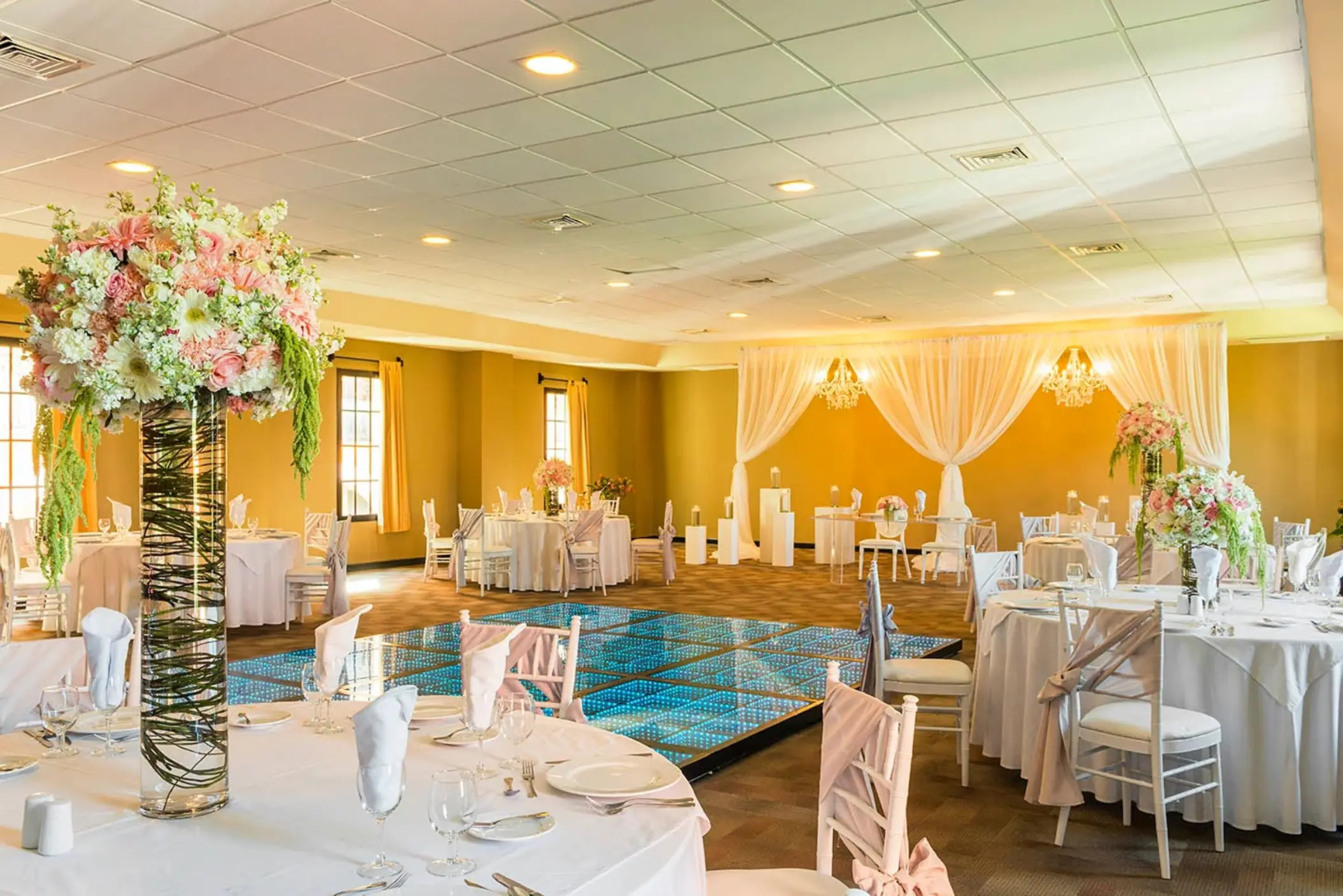 A reception hall decorated for an event, featuring tables with floral centerpieces and a dance floor.