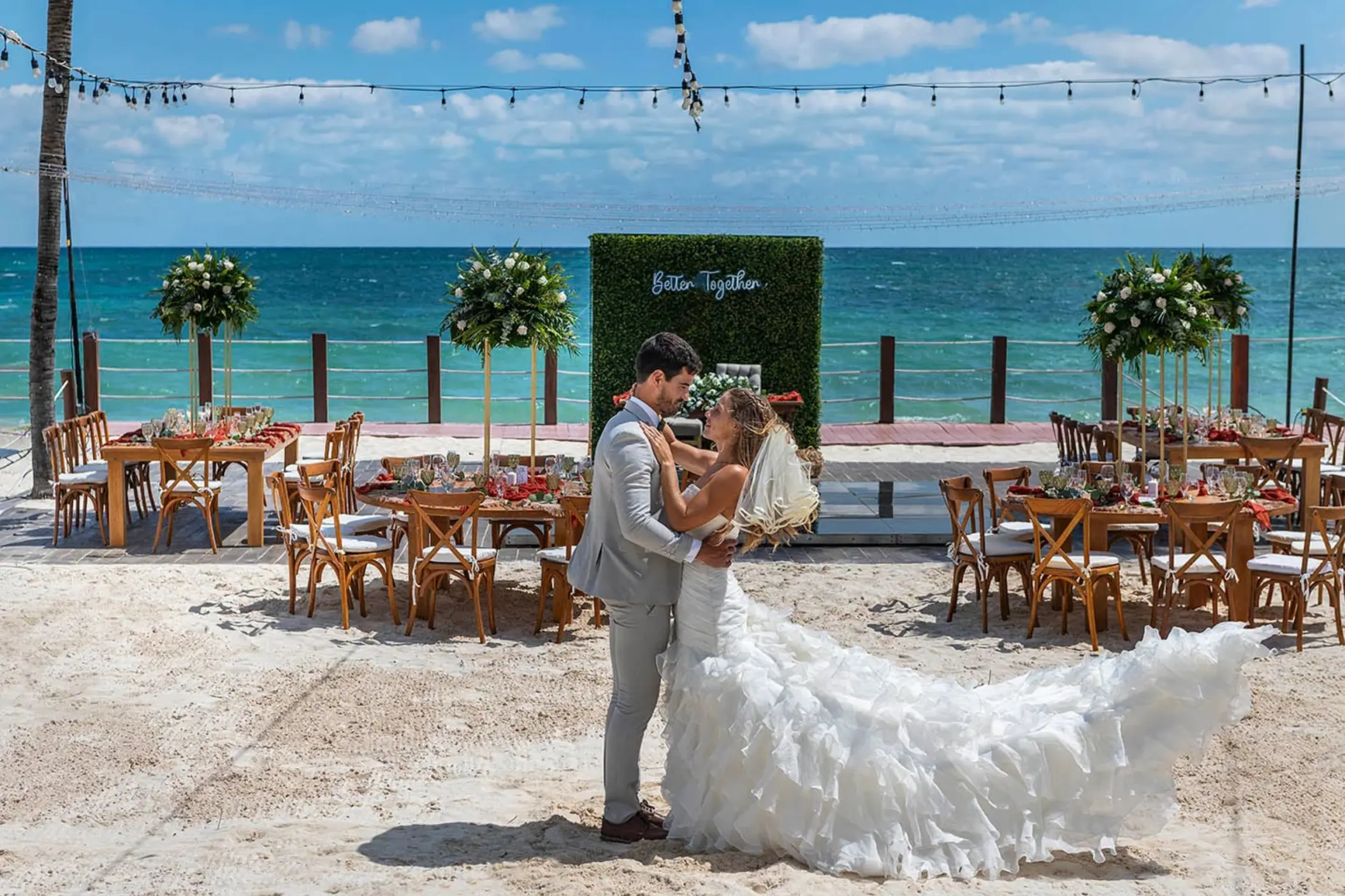 newlywed couple embraces on a white sand beach with turquoise ocean in the background and a 