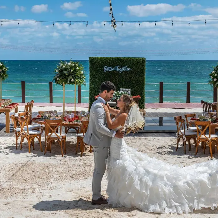 newlywed couple embraces on a white sand beach with turquoise ocean in the background and a 