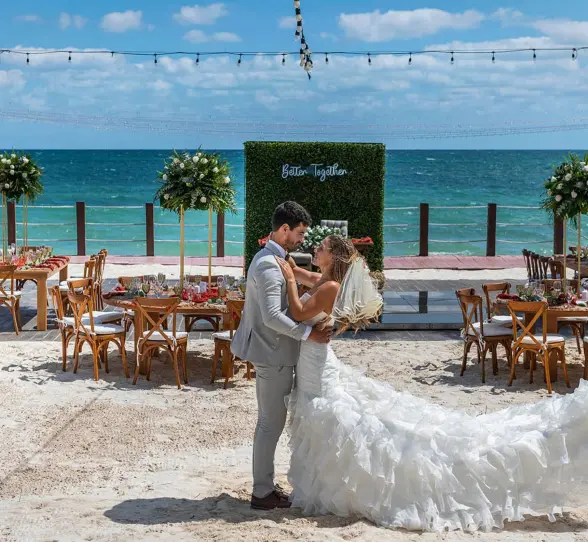 newlywed couple embraces on a white sand beach with turquoise ocean in the background and a 