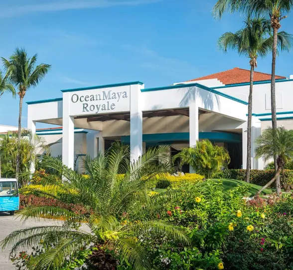The main entrance of Ocean Maya Royale resort, featuring a grand white building, lush tropical landscaping, and a blue golf cart.
