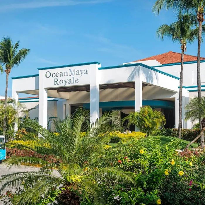 The main entrance of Ocean Maya Royale resort, featuring a grand white building, lush tropical landscaping, and a blue golf cart.