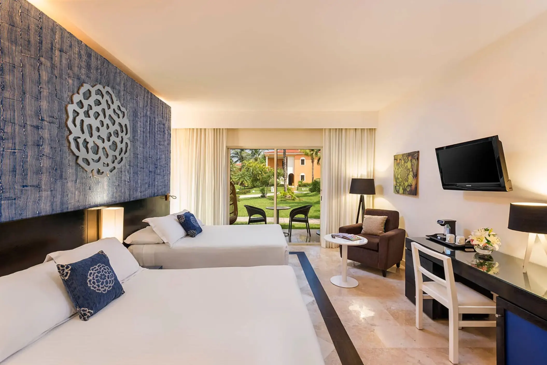 spacious Maya Superior Deluxe room with two beds, a blue accent wall, a seating area, and a balcony overlooking the resort grounds.