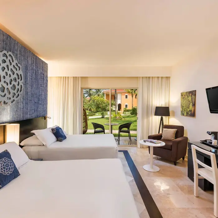 spacious Maya Superior Deluxe room with two beds, a blue accent wall, a seating area, and a balcony overlooking the resort grounds.