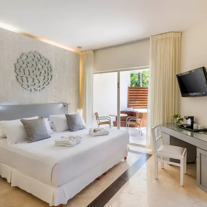A stylish honeymoon deluxe room with a large bed, modern decor, and a private balcony featuring a hot tub for two.