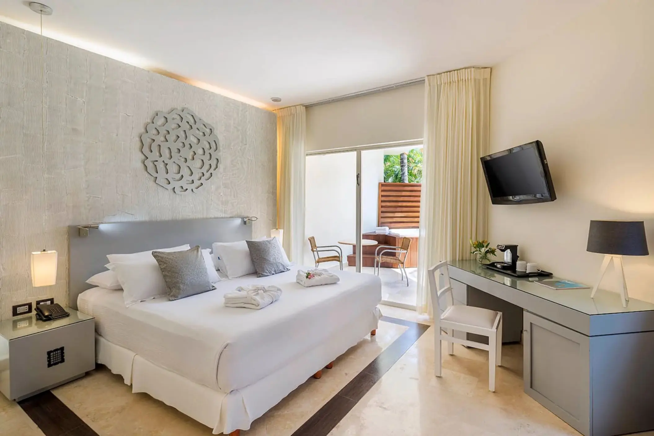 A stylish honeymoon deluxe room with a large bed, modern decor, and a private balcony featuring a hot tub for two.