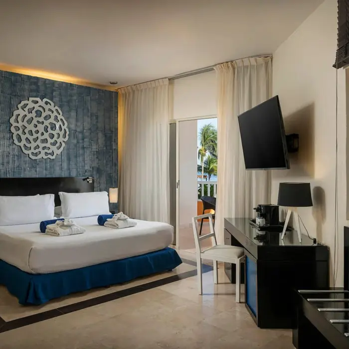 bright oceanfront suite with a king bed, blue patterned wall, wooden blinds, and a balcony overlooking the ocean.