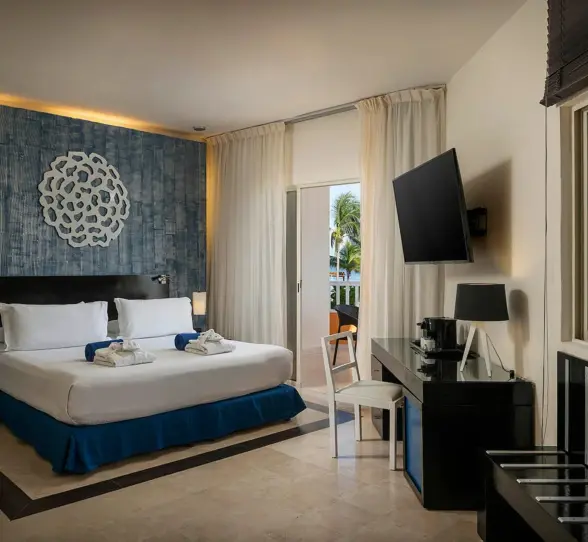bright oceanfront suite with a king bed, blue patterned wall, wooden blinds, and a balcony overlooking the ocean.