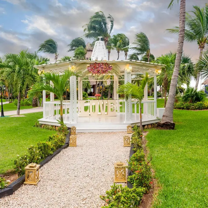 beautiful outdoor wedding gazebo on a lush green lawn, adorned with pink flowers and surrounded by palm trees